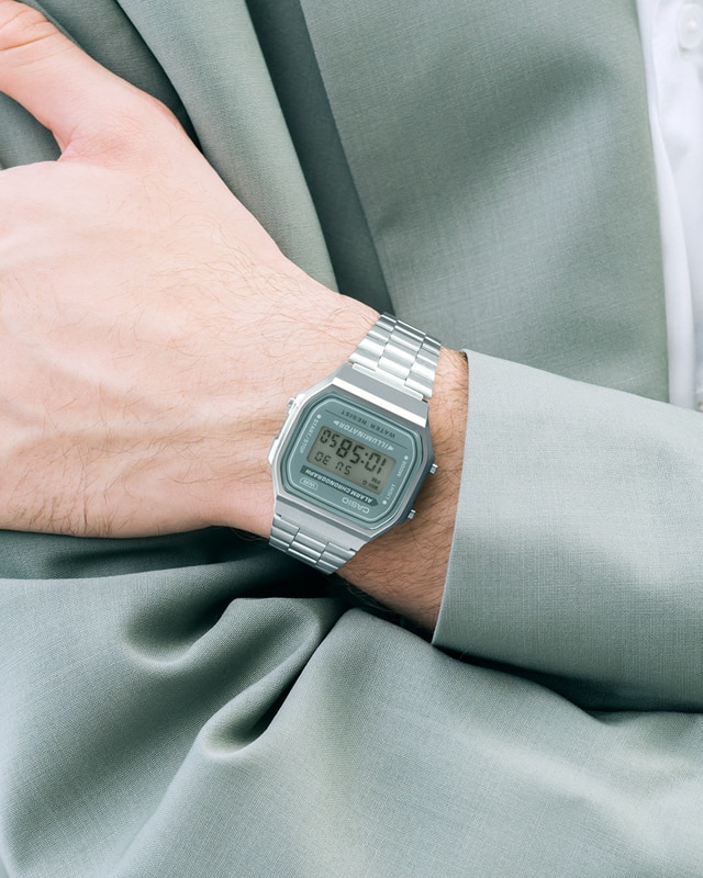 L'orologio digitale Casio Vintage Collection A168WA-3AY con cinturino argentato e cornice grigia sul display al polso di un uomo con giacca grigia