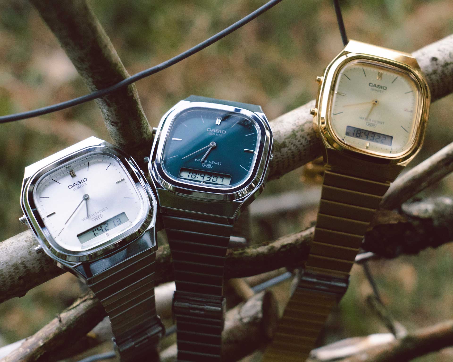 Tre orologi della CASIO Vintage Collection appesi a un albero, due con bracciale metallico argento e uno con quadrante e bracciale dorati.