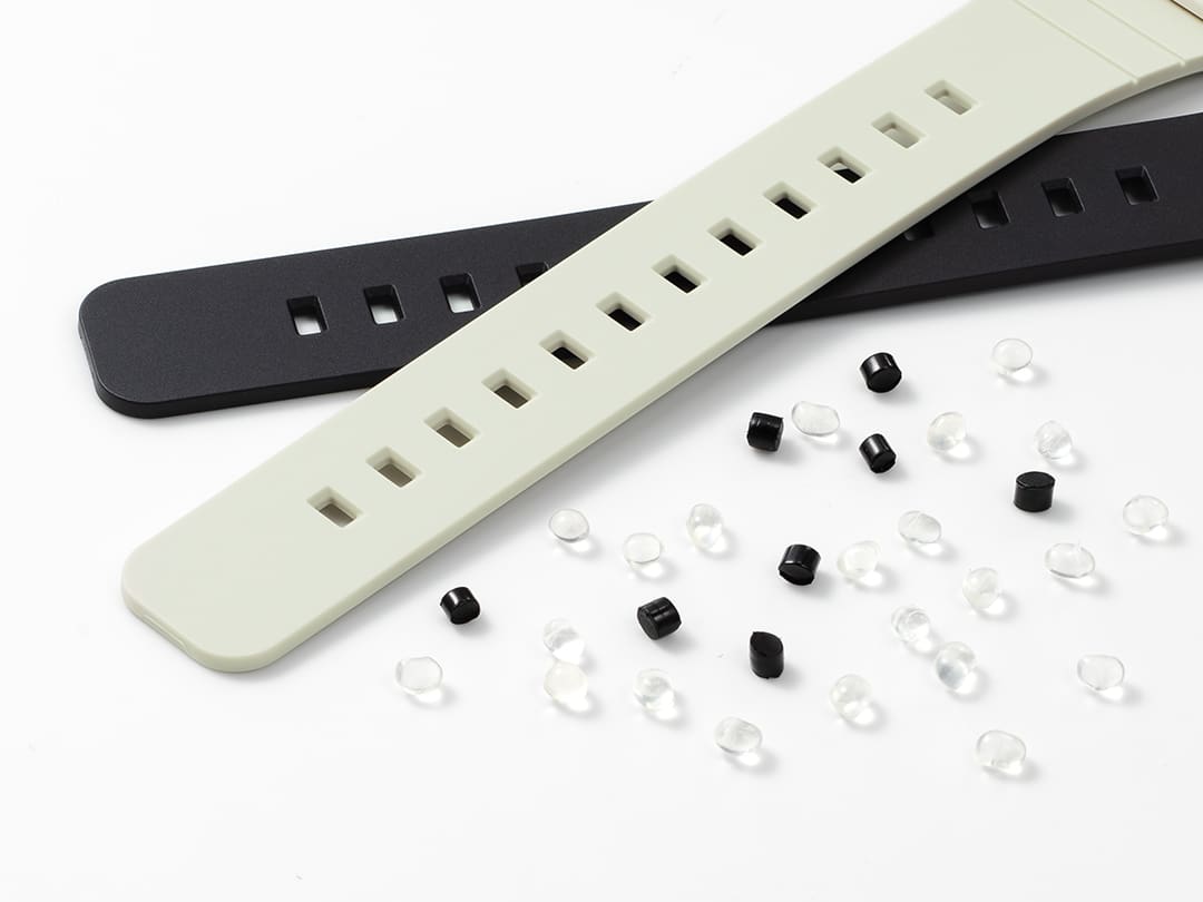 Un cinturino nero e uno bianco antico sono disposti in diagonale l'uno sull'altro accanto a piccole parti in plastica nera e trasparente su sfondo bianco