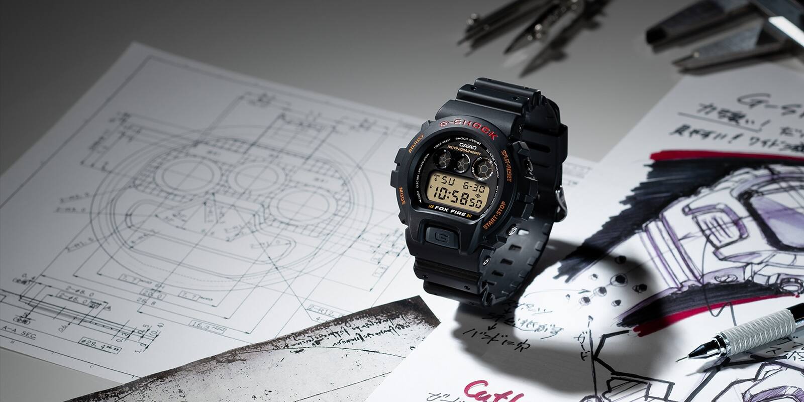 L'orologio da polso Casio G-Shock DW-6900B-9 su un tavolo pieno di disegni concettuali, oltre a una penna, una bussola e uno strumento di misurazione