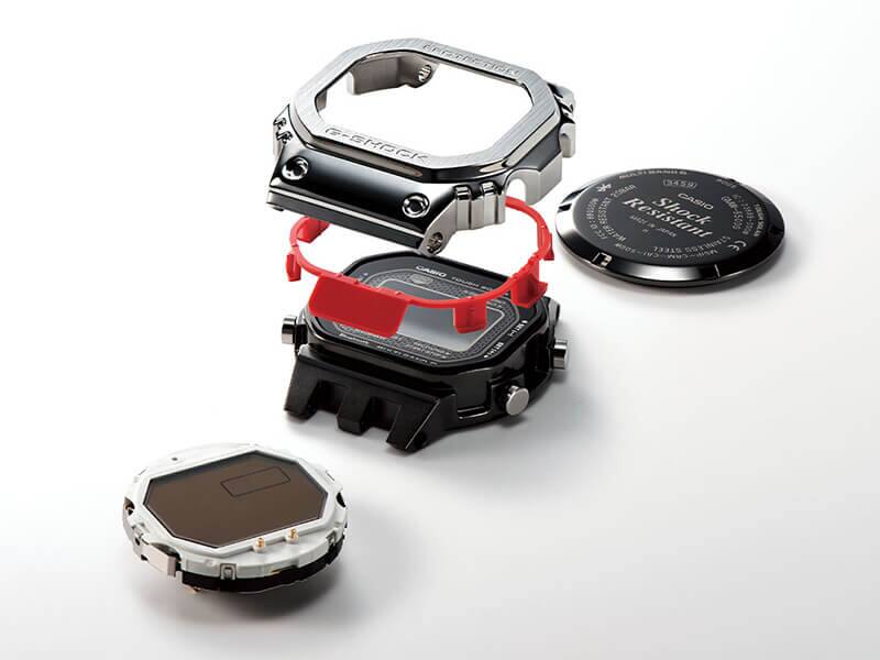 Cassa, componente tampone rosso e lunetta in titanio argentato dell'orologio digitale GMW-B5000D-1 mostrati separatamente l'uno sull'altro, con il fondello e il display accanto