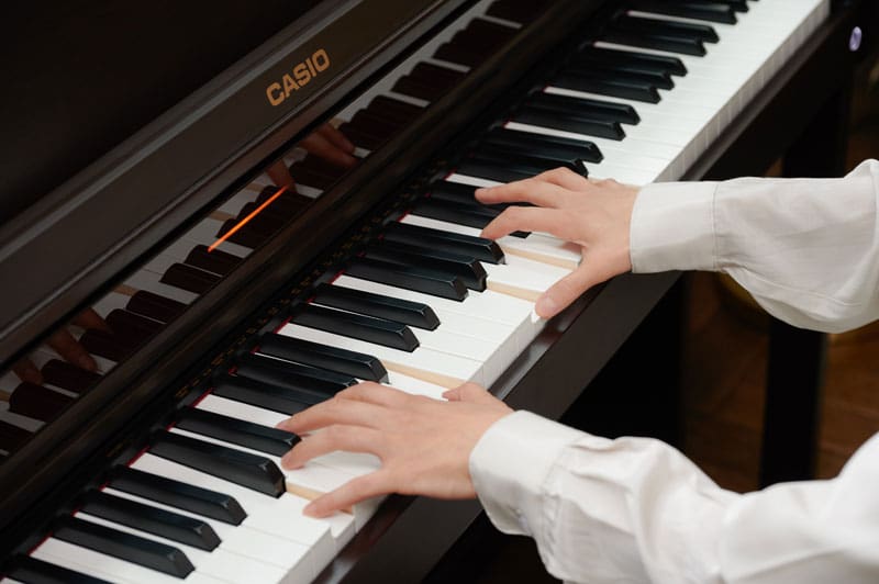 Mani che suonano il pianoforte su un pianoforte digitale Casio AP-550BK