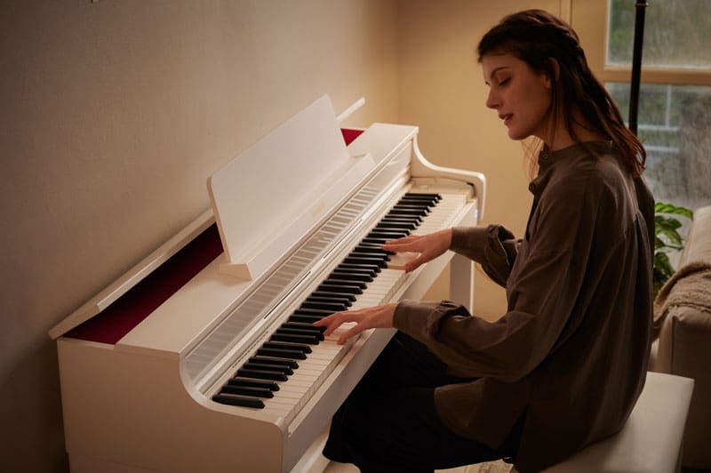 Una donna siede al pianoforte digitale CELVIANO AP-550WE bianco e suona il pianoforte