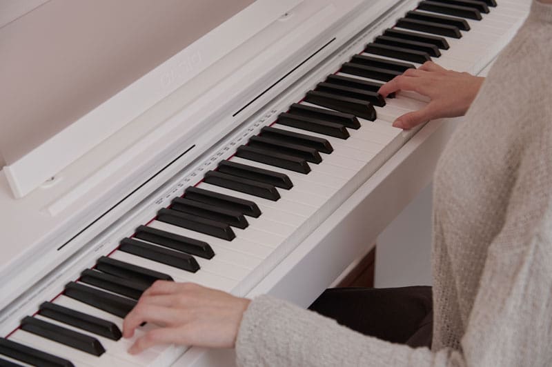 Primo piano di due mani che suonano il pianoforte su un pianoforte digitale Celviano AP-S200WE bianco