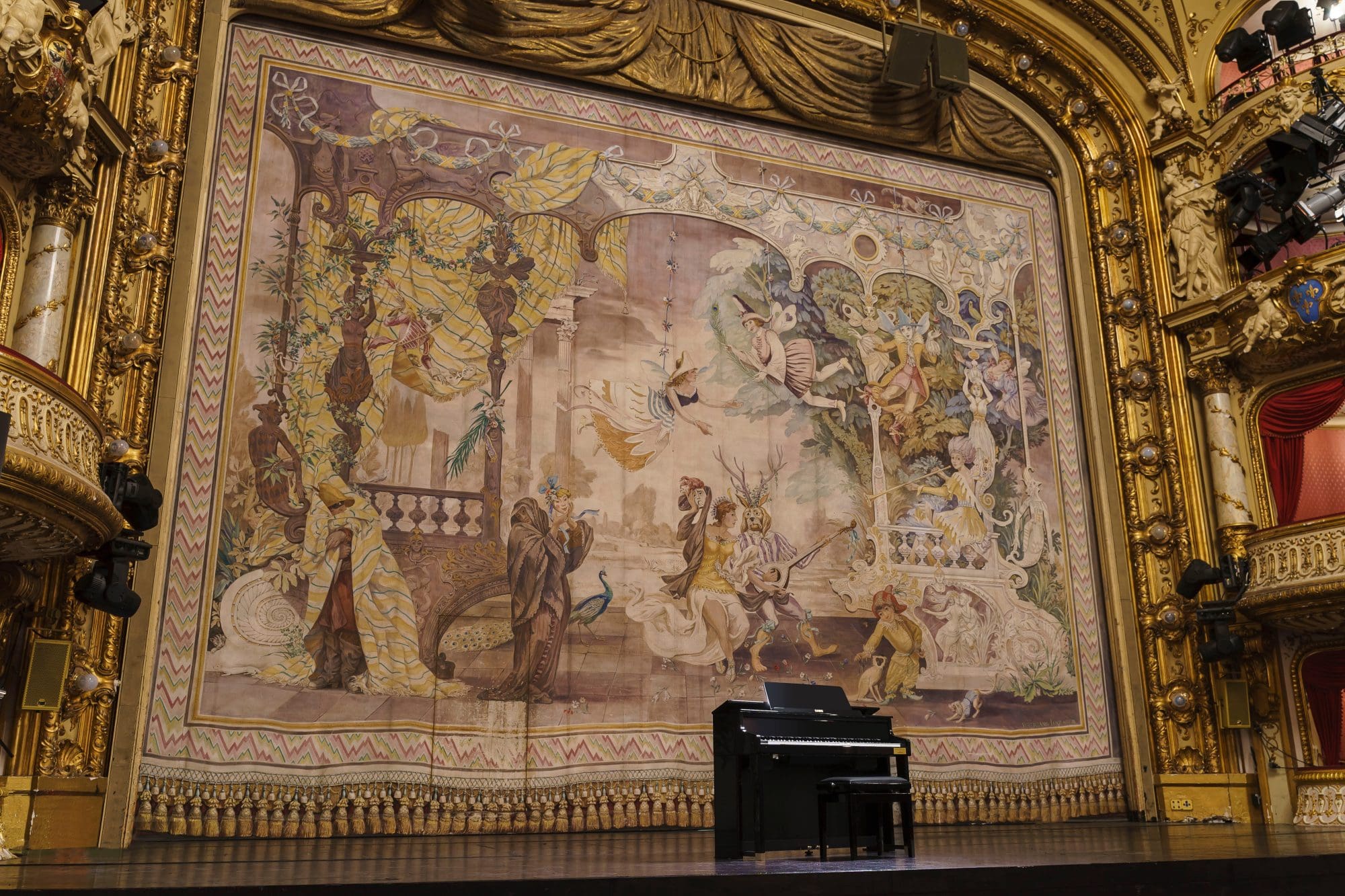 Il pianoforte digitale CELVIANO Grand Hybrid GP-510BP, di colore nero, si trova da solo su un grande palco da concerto, davanti a un imponente sipario che ricorda un arazzo medievale.