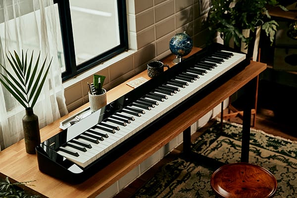 Il pianoforte digitale Privia PX-S5000 su una stretta scrivania di legno davanti a una finestra