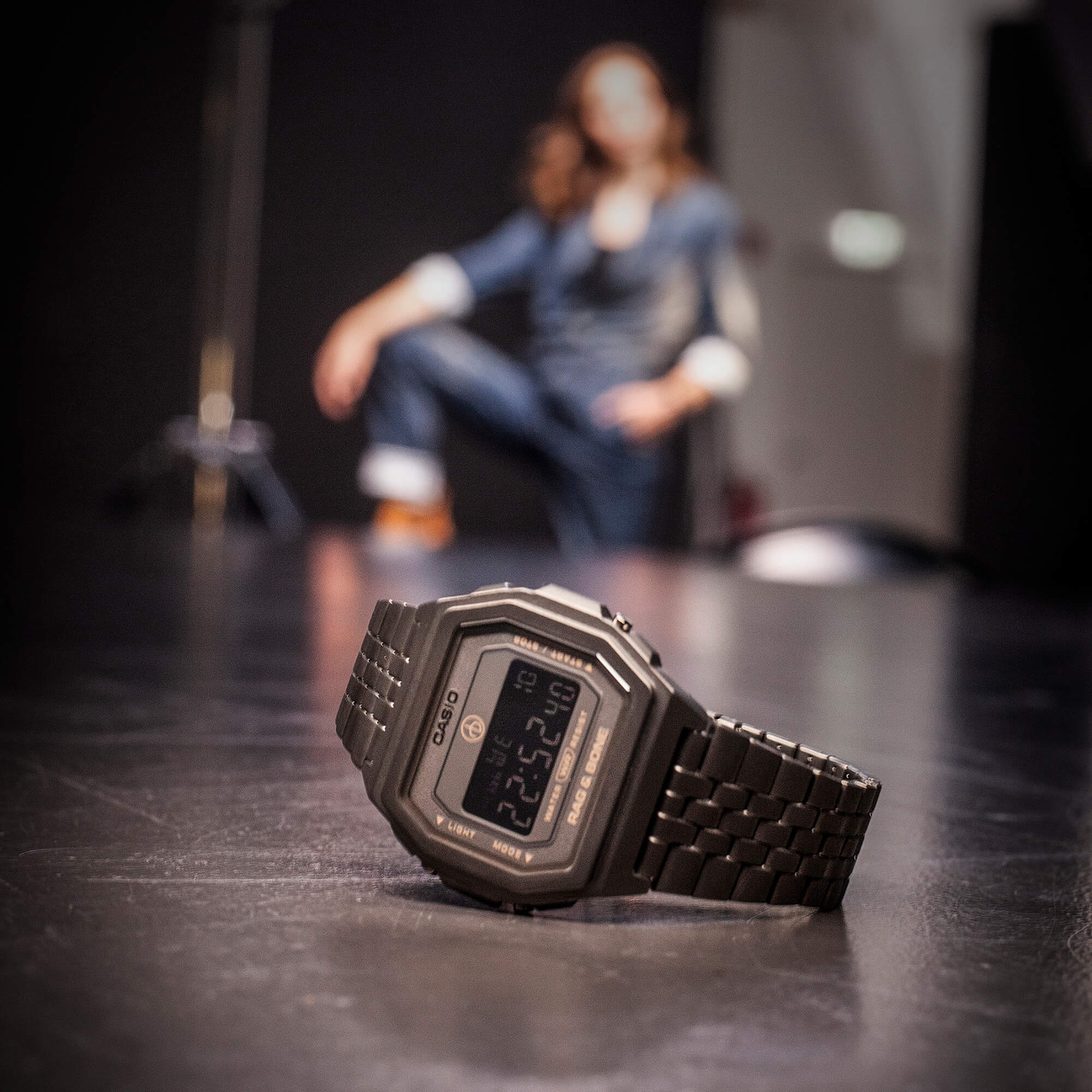 L'A1000RCG-8B di Casio Vintage giace su un tavolo nero, sullo sfondo si intravede una donna.