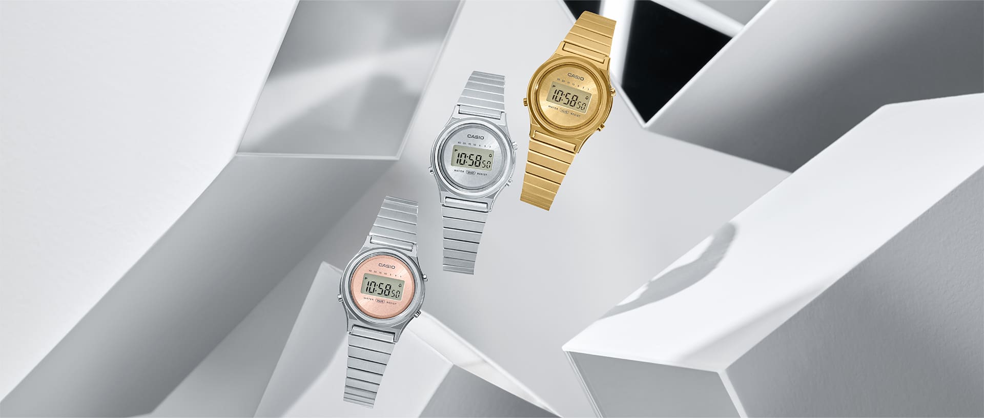 Tre orologi digitali su uno sfondo grigio astratto: il modello LA700WE-4A con cinturino argentato e display rosa, il modello LA700WE-7A con cinturino argentato e display argentato e il modello LA700WEG-9A con cinturino dorato e display dorato.