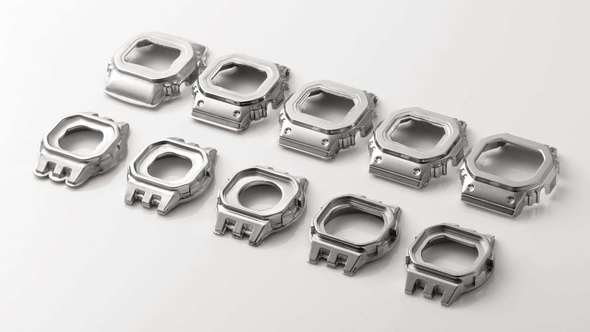 Tien zilverkleurige bezels in verschillende stadia van productie - van de lege tot de afgewerkte bezel van het Casio G-Shock GMW-B5000D digitale horloge
