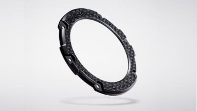 Koolstof bezel van een Casio G-Steel GST-B100 polshorloge tegen een lichtgrijze achtergrond