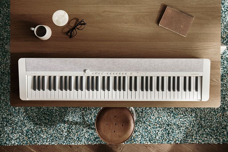 Bovenaanzicht van een witte CT-S1-76WE digitale piano op een bruin tafelblad