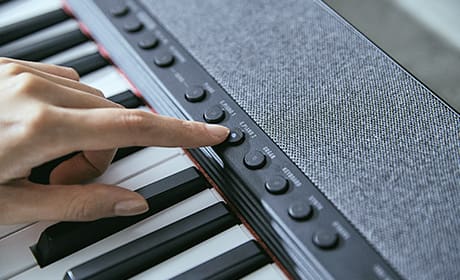 Close-up van het toetsenbord en het bedieningspaneel van een Casiotone CT-S1 digitale piano, een vinger drukt op een knop op het bedieningspaneel
