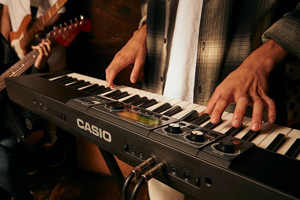 Zicht van achteren op een Casiotone CT-S500 en de verschillende aansluitmogelijkheden terwijl iemand het toetsenbord bespeelt