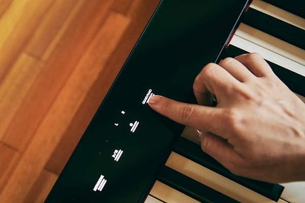 Close-up van de touchbediening van de zwarte Privia PX-S1100BK digitale piano, een vinger raakt een touchveld aan