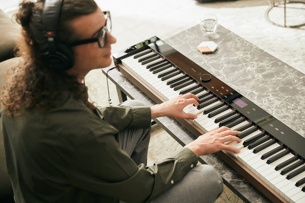 Een jonge man draagt een koptelefoon en bespeelt de PX-S6000 digitale piano voor hem op de tafel in de woonkamer