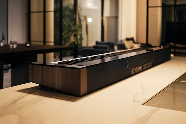 Zicht op de achterkant en een hoek van de PX-S6000 digitale piano, waar de zwarte lange zijde en de smalle zijde met walnoot houtnerf elkaar ontmoeten