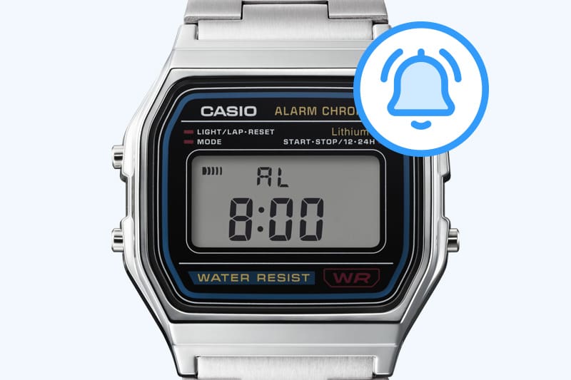 Um ícone de alarme azul ao lado do visor do relógio de pulso digital prateado.