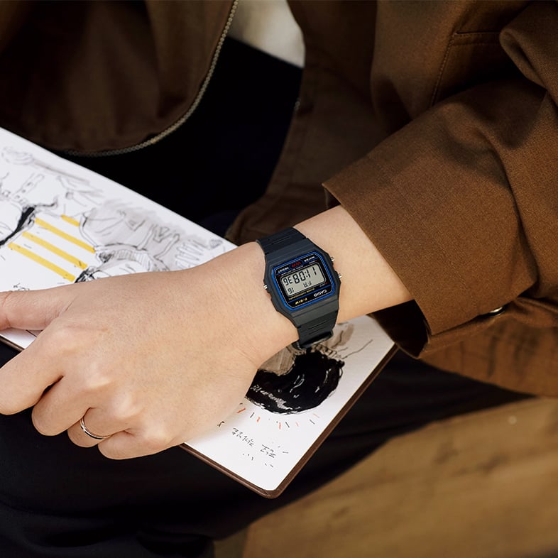 O F-91W-1 no pulso de uma mulher, com um caderno visível por baixo do pulso.