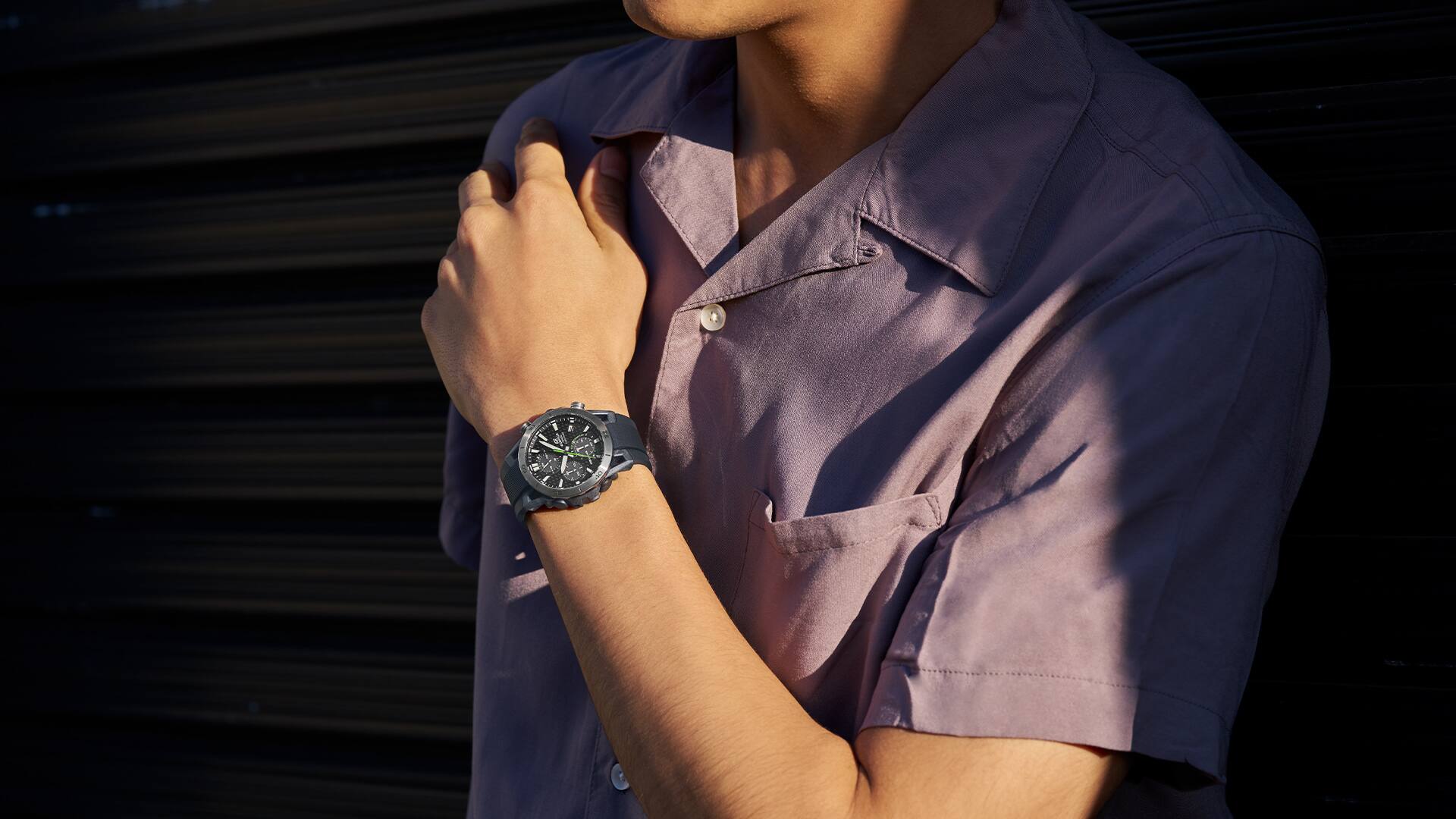 Um relógio de pulso Casio Edifice no pulso de um homem com uma camisa lilás