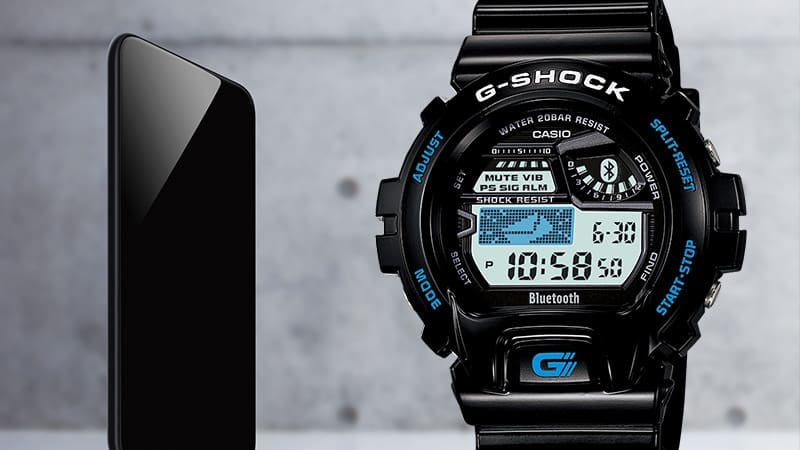 À esquerda: Um smartphone, à direita: o relógio de pulso preto Casio G-Shock GB-6900-1 