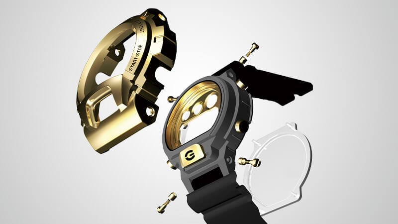 Os componentes da caixa de um modelo Casio G-Shock DW-6900 com luneta metálica dourada e bracelete preta