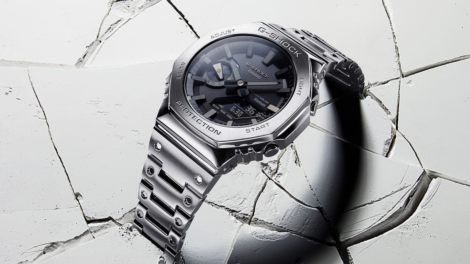 O relógio Casio G-Shock GM-B2100D prateado em aço inoxidável com mostrador preto tem uma bracelete em gesso escovado