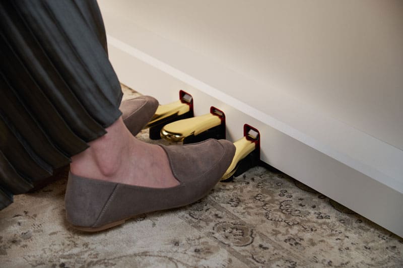 Dois pés de mulher em mocassins cinzentos mate a acionar os pedais dourados de um piano digital AP-300 branco