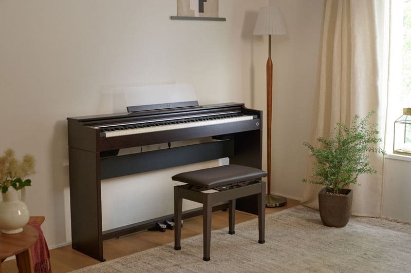 Um piano digital CASIO AP-S200BN castanho está encostado à parede de uma sala de estar com um banco de piano a condize