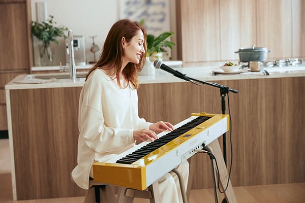 Uma mulher senta-se no piano digital PX-S7000HM, toca piano e canta para um microfone
